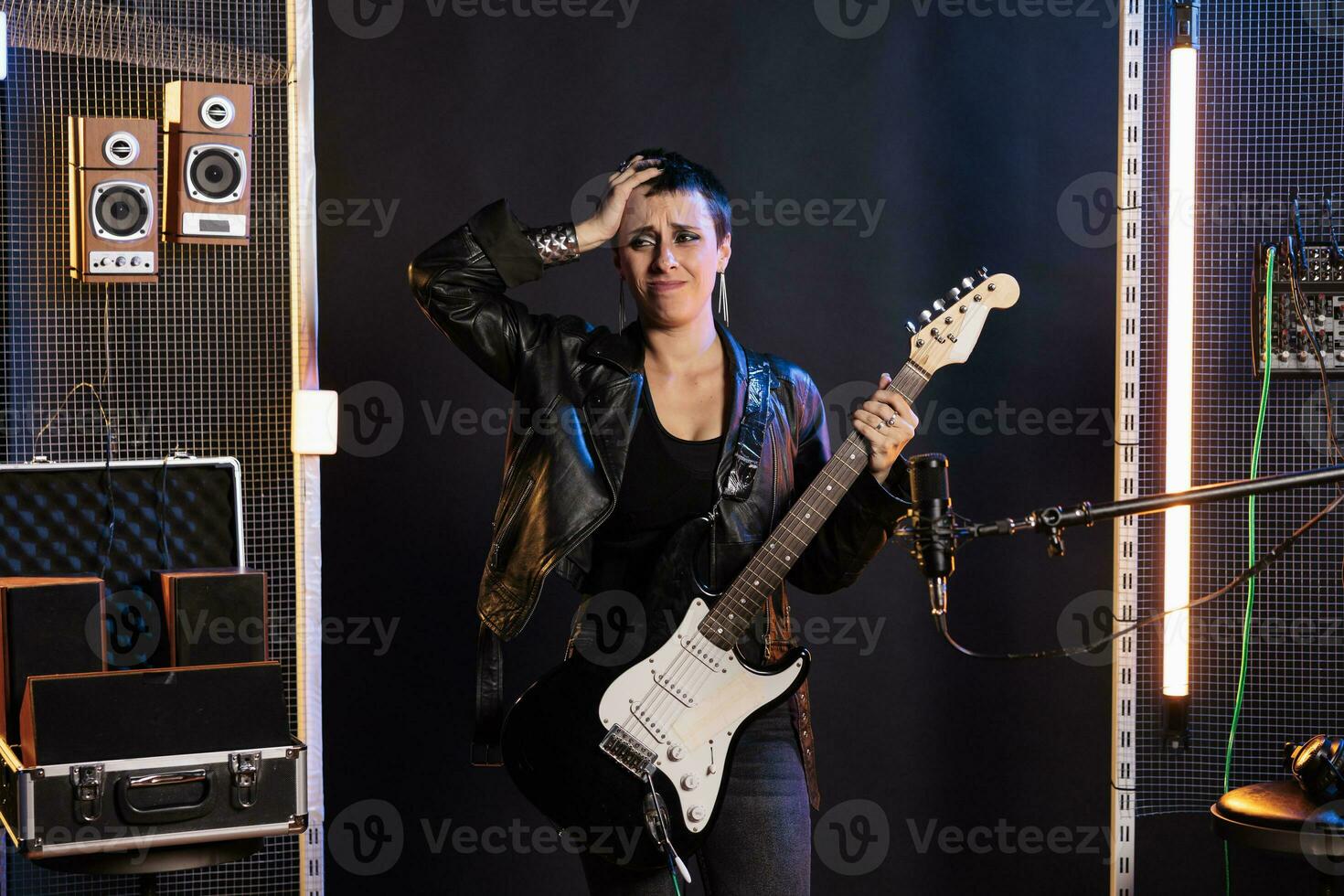 irritato stella del rock dimenticare il roccia canzone mentre giocando a elettrico chitarra preparazione per grunge concerto nel suono studio, Lavorando a nuovo album. superstar donna nel pelle attrezzatura utilizzando strumento elettrico foto