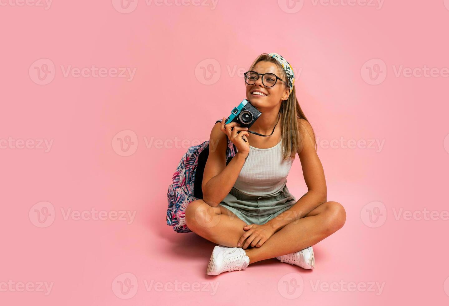 sorridente biondo donna nel bianca superiore e pantaloncini in posa con telecamera su rosa sfondo. estate stile di vita. viaggio concetto. foto