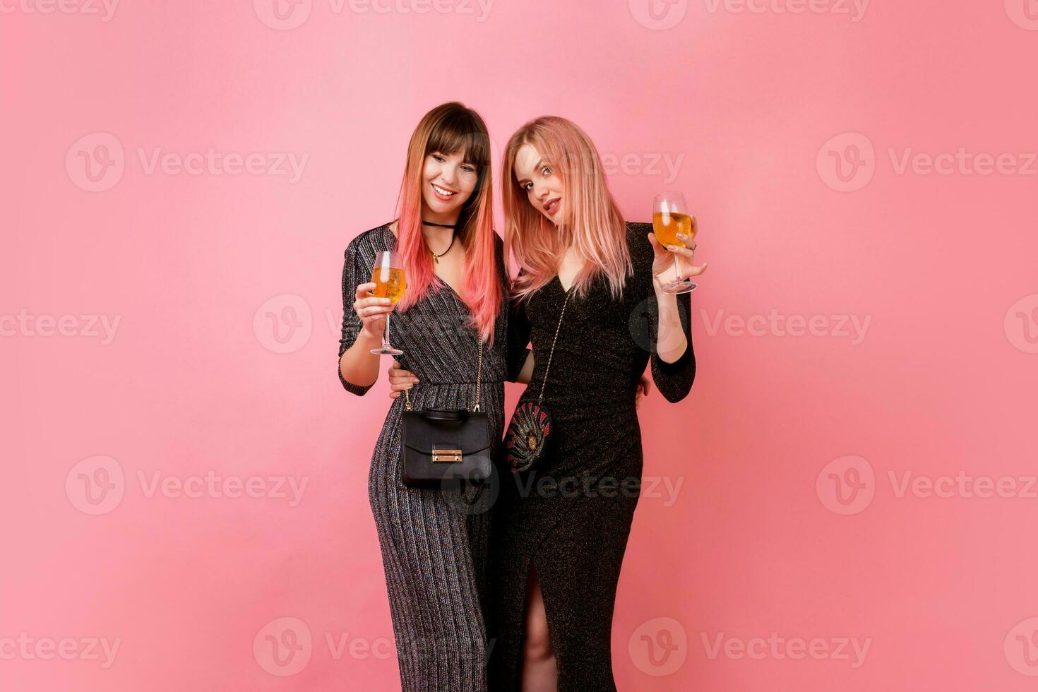 elegante ragazze con bicchieri di alcool bevande in posa su leggero rosa sfondo. festa umore. indossare lusso paillettes vestito . foto