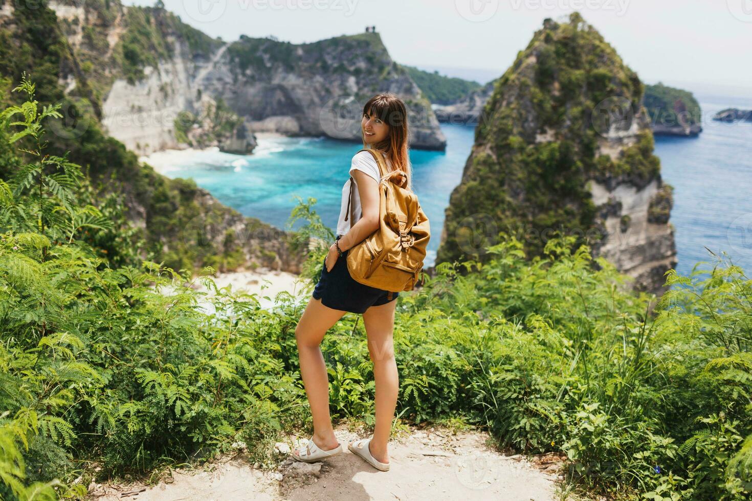 indietro Visualizza di in viaggio donna in piedi su scogliere e tropicale spiaggia sfondo. la libertà e avventura concetto. pieno lunghezza. Indonesia, nusa penida isola. foto