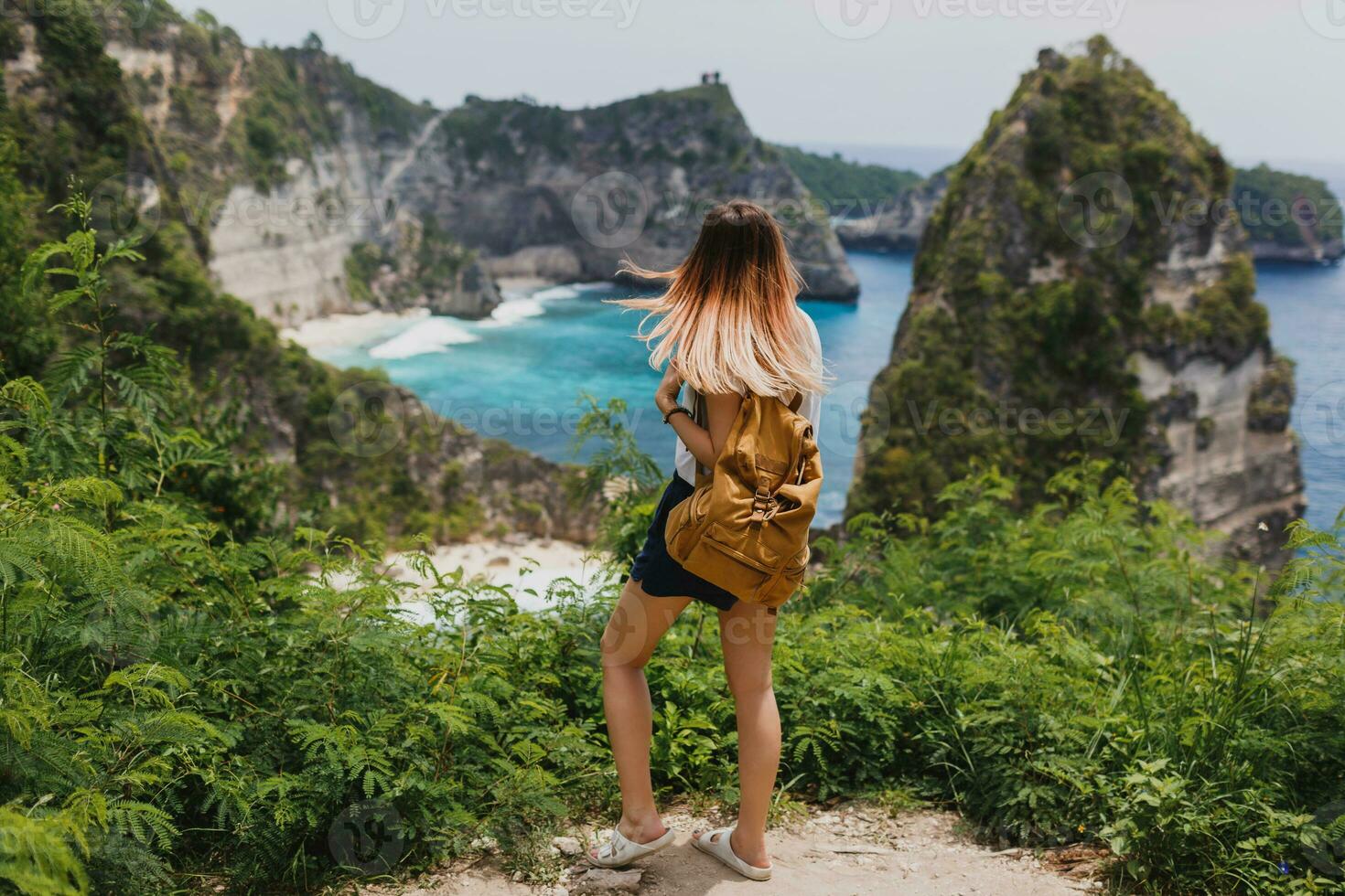 indietro Visualizza di in viaggio donna in piedi su scogliere e tropicale spiaggia sfondo. la libertà e avventura concetto. pieno lunghezza. Indonesia, nusa penida isola. foto