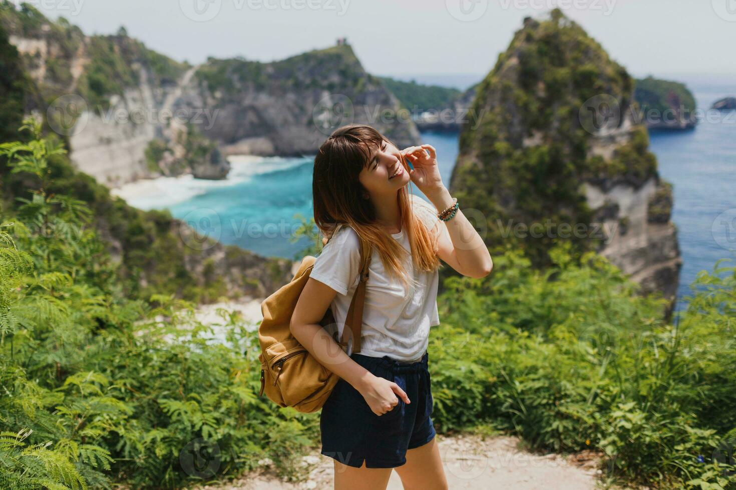 in viaggio e avventura concetto. contento bella donna con indietro imballare in viaggio nel Indonesia su nusa penida isola. sorprendente scogliere e tropicale spiaggia Visualizza su sfondo. foto