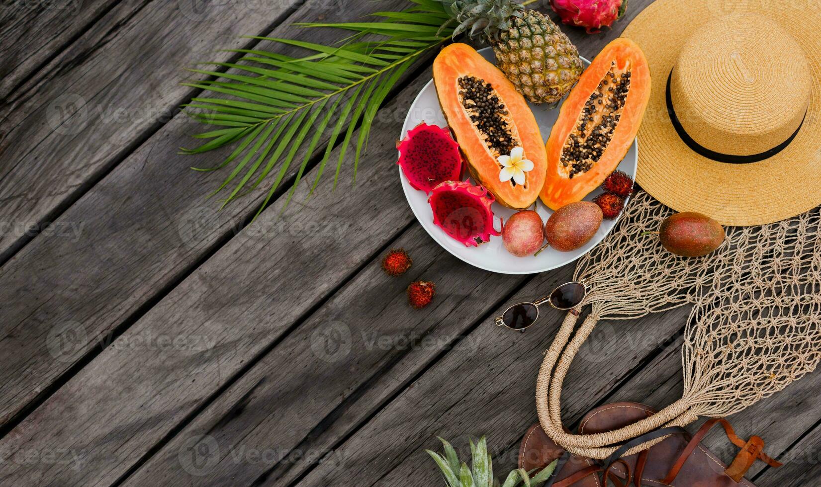 estate tropicale composizione. verde palma le foglie e tropicale frutta su legna sfondo. piatto posizione, superiore Visualizza. cannuccia cappello e uncinetto intrecciata Borsa. foto