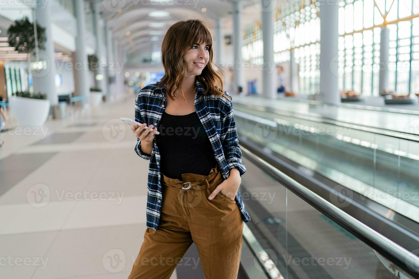 femmina a piedi attraverso il aeroporto utilizzando sua smartphone dispositivo. foto