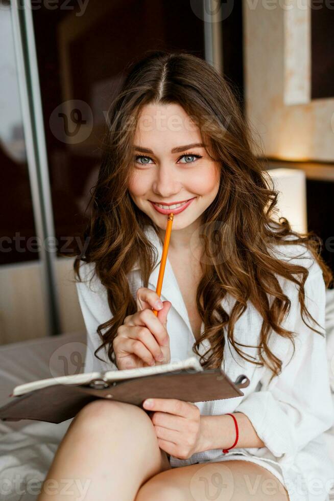 vicino su stile di vita ritratto di giovane bellissimo donna nel bianca camicia sorridente e guardare a telecamera. accogliente caldo casa atmosfera. foto