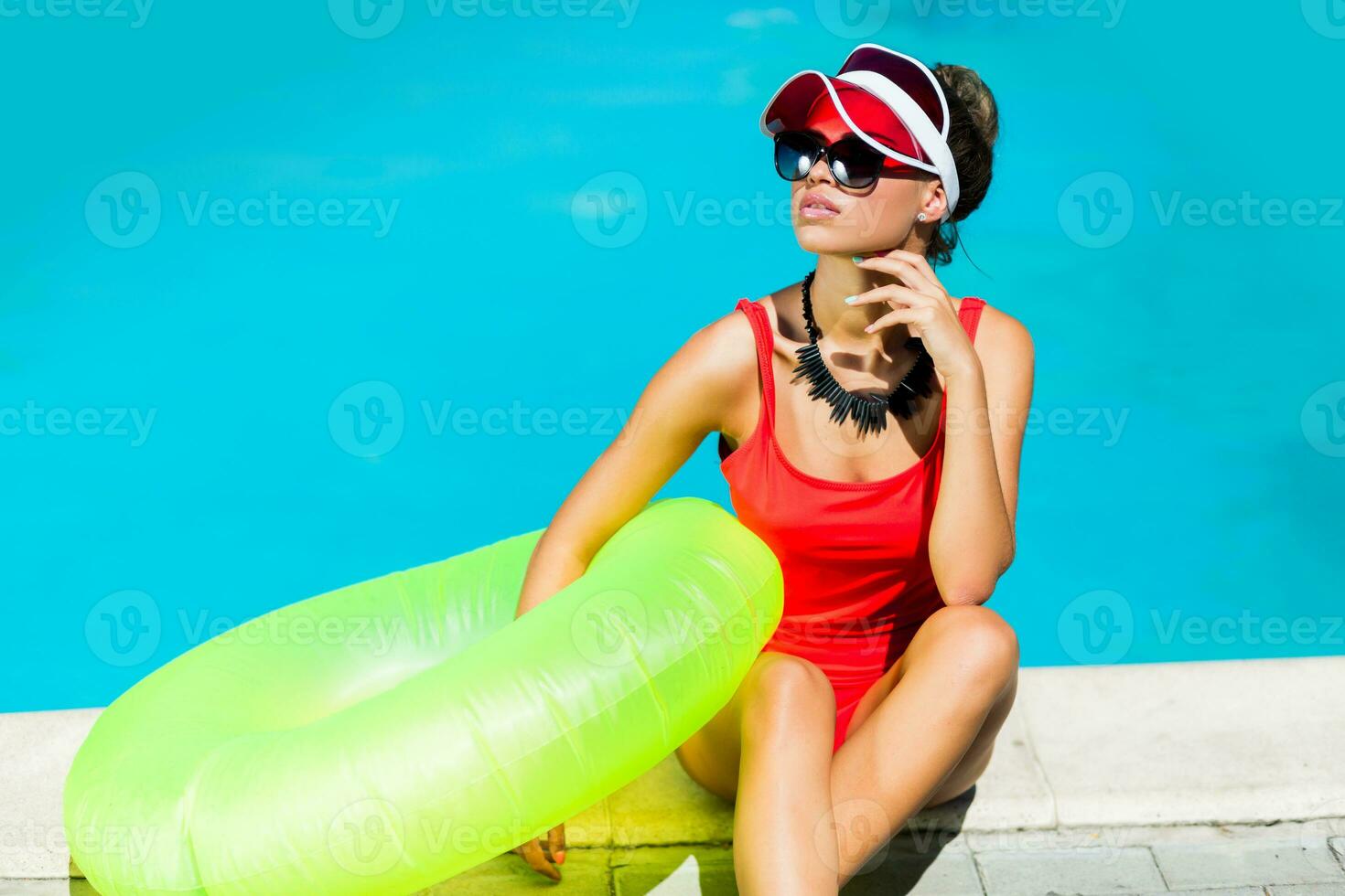 sexy abbronzato donna nel rosso costume da bagno avendo divertimento e godendo estate nel sorprendente grande nuoto piscina. elegante trasparente cap. spiaggia festa. foto