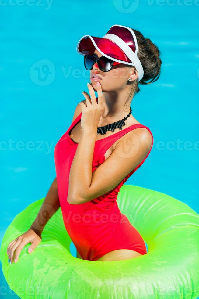 sexy abbronzato donna nel rosso costume da bagno avendo divertimento e godendo estate nel sorprendente grande nuoto piscina. elegante trasparente cap. spiaggia festa. foto