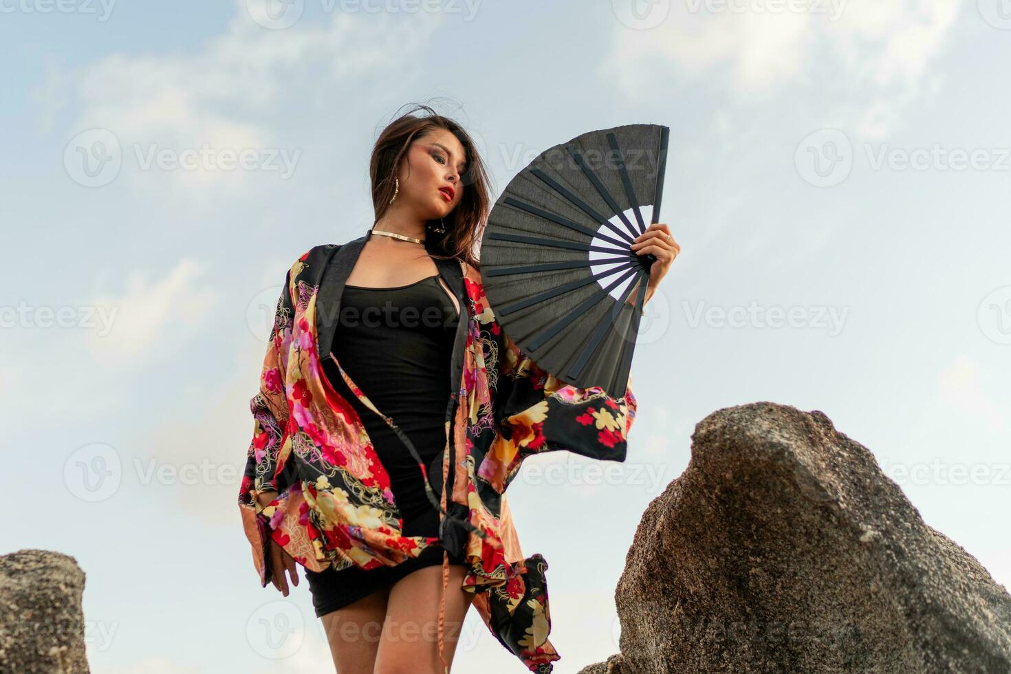 sensuale asiatico donna nel seta chimono Tenere fan e in posa al di sopra di rocce su il spiaggia. foto
