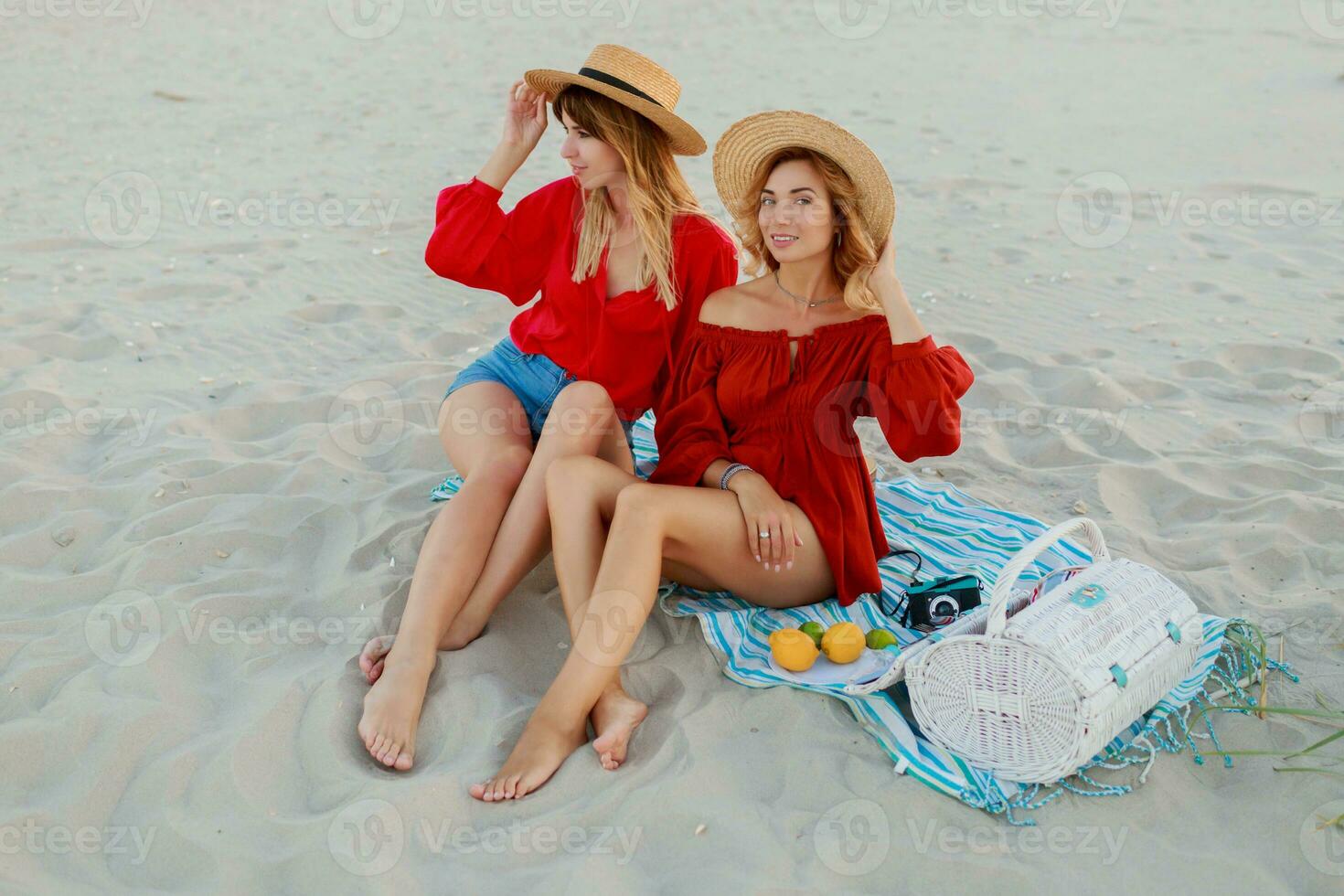 Due bella donne nel rosso estate attrezzatura abd cannuccia cappelli godendo picnic su il spiaggia. estate umore. foto