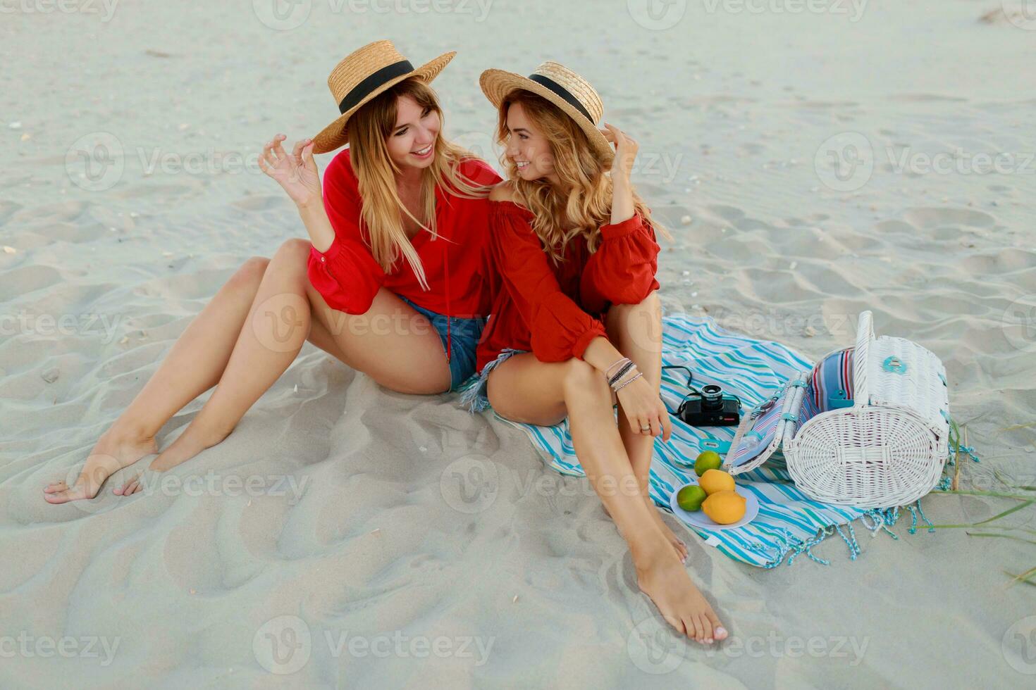 Due bella donne nel rosso estate attrezzatura abd cannuccia cappelli godendo picnic su il spiaggia. estate umore. foto