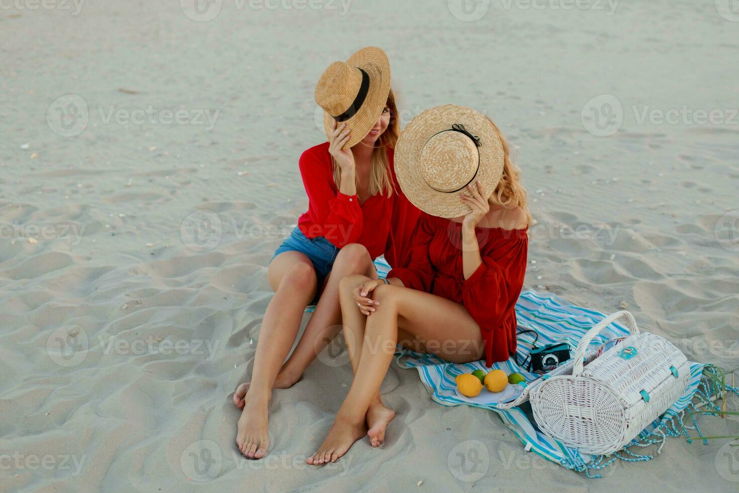 Due bella donne nel rosso estate attrezzatura abd cannuccia cappelli godendo picnic su il spiaggia. estate umore. foto