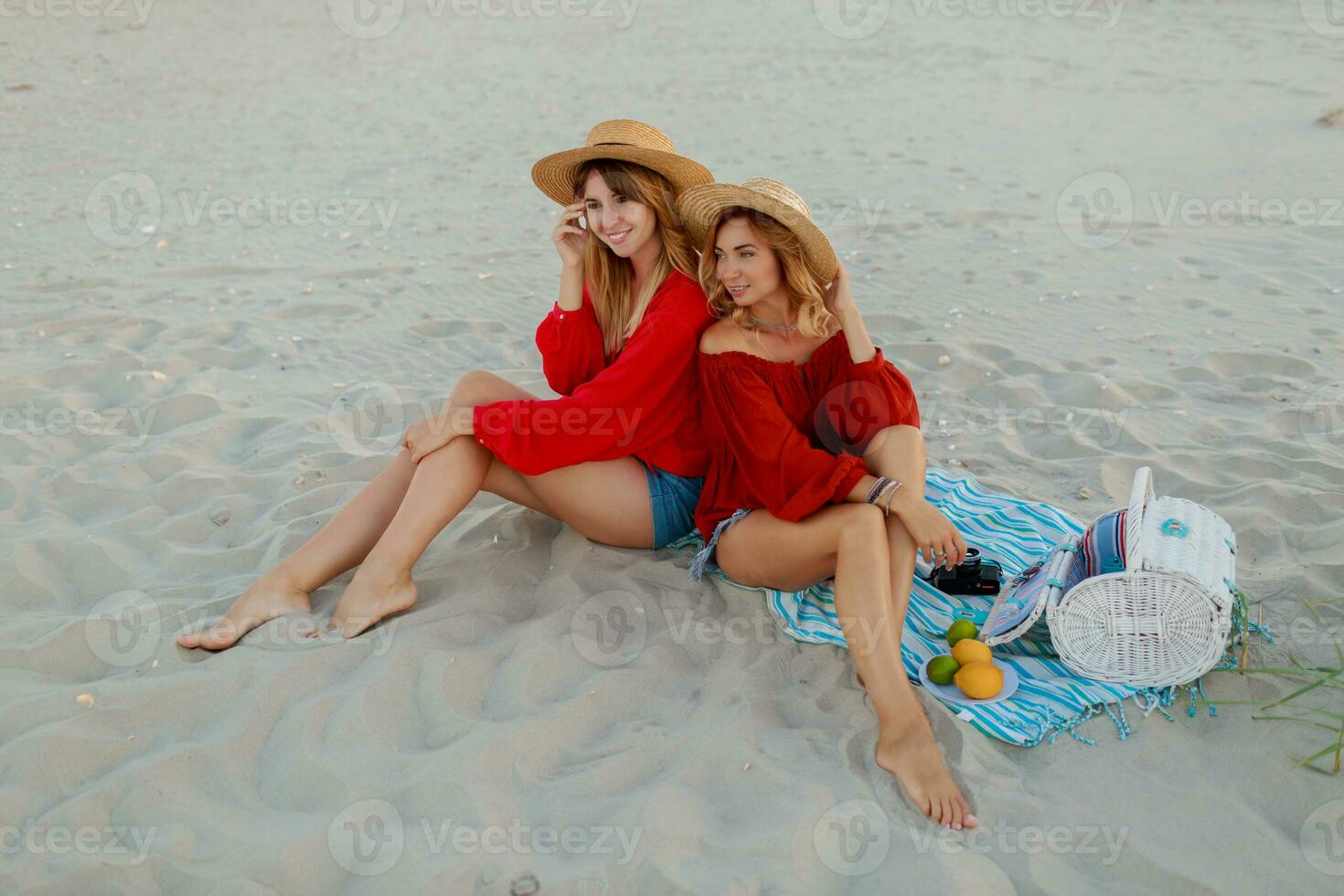 Due bella donne nel rosso estate attrezzatura abd cannuccia cappelli godendo picnic su il spiaggia. estate umore. foto