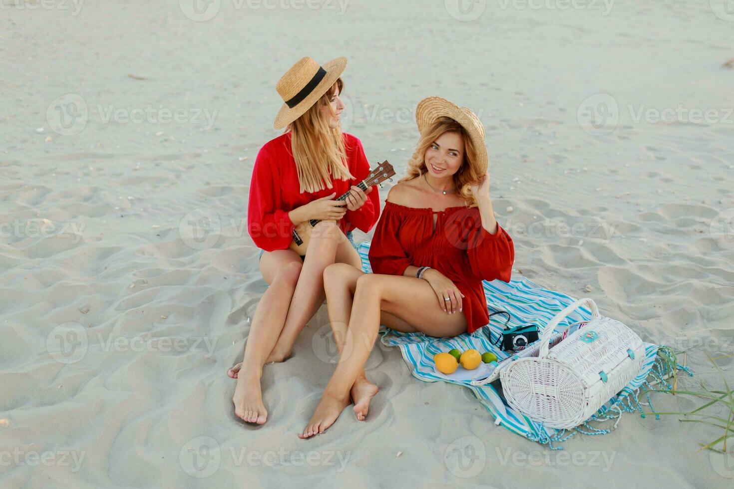 Due bella donne nel rosso estate attrezzatura abd cannuccia cappelli godendo picnic su il spiaggia. estate umore. foto