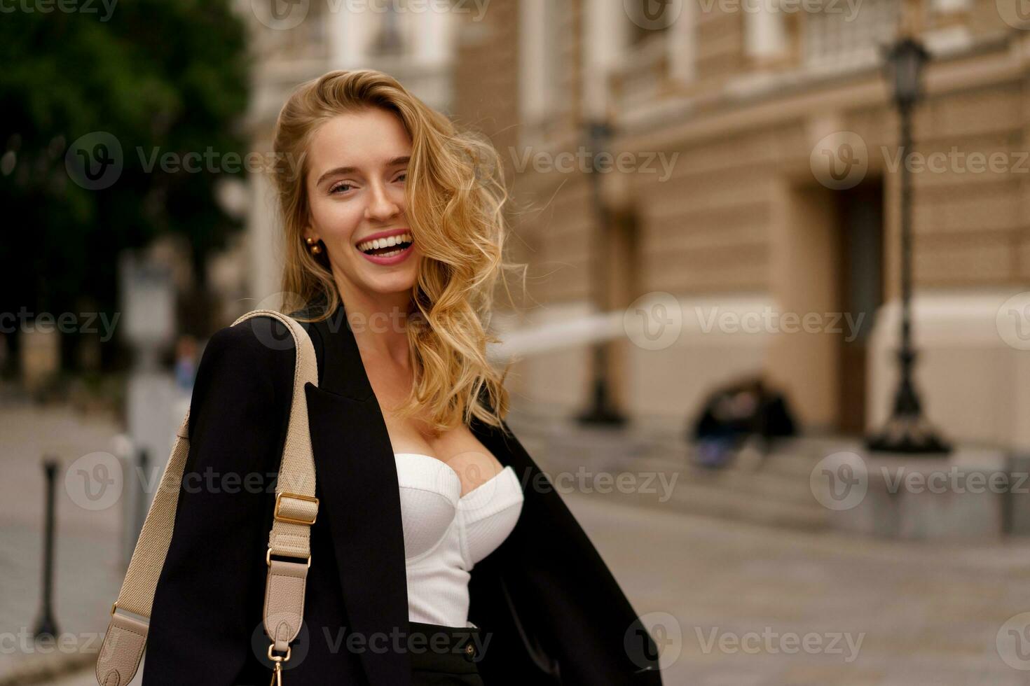 bellissimo sorridente donna nel elegante nero completo da uomo in posa all'aperto nel vecchio europeo città. biondo ondulato capelli, perfetto pelle. foto