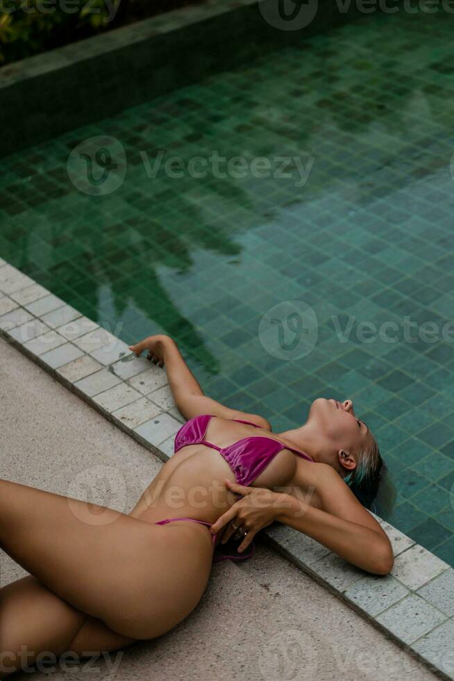 bellissima biondo donna nel sensuale rosa costumi da bagno in posa vicino piscina su lusso tropicale villa. foto