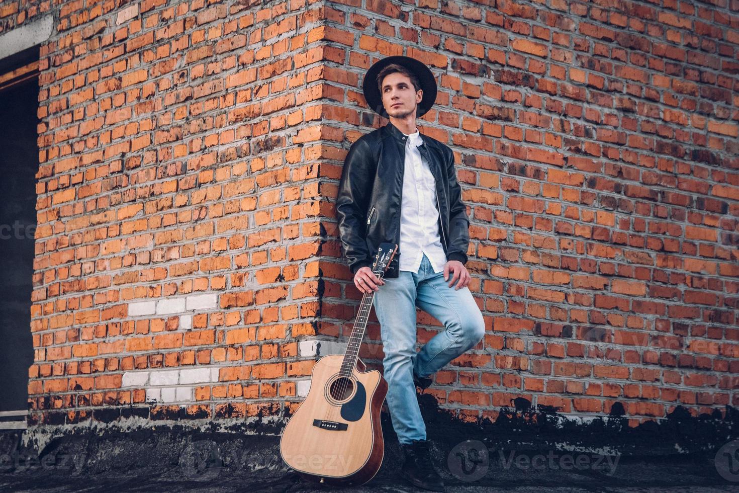 uomo con una chitarra sullo sfondo di un muro di mattoni foto