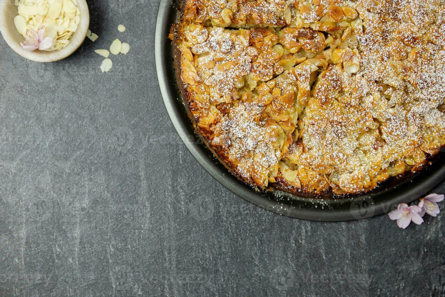 mandorla fatti in casa torta con affettato mandorle Crosta e glassatura polvere zucchero su buio sfondo. superiore Visualizza. copia spazio. foto