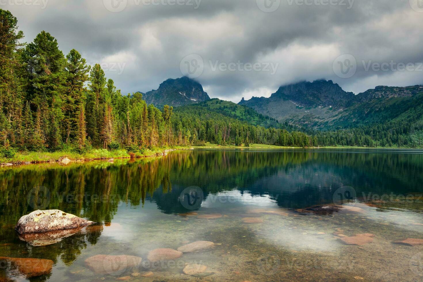 pittoresco riva di un' montagna lago con cedri sotto un' drammatico cielo. taiga rocce con blu cielo nel il caldo sole e alberi montagna soleggiato paesaggio. ergaki natura parco nel il montagne di Siberia. foto