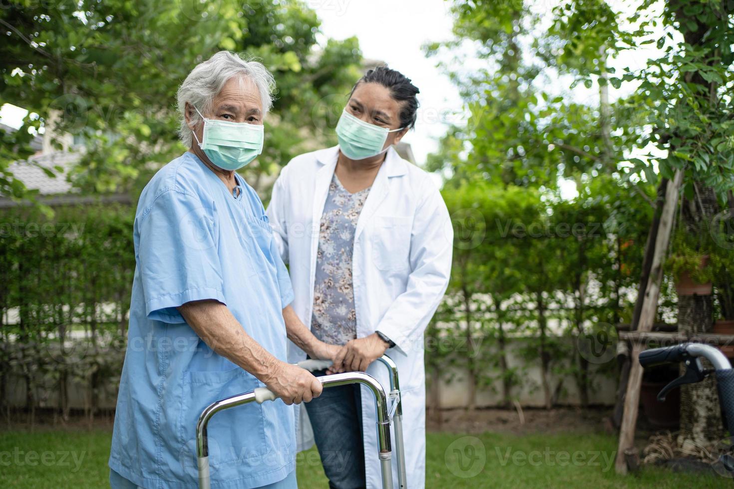 medico aiuta e cura la donna anziana asiatica usa il camminatore nel parco. foto