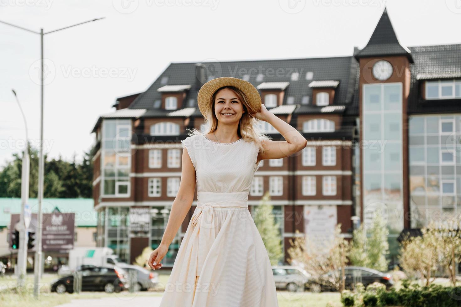 una bella bionda cammina per una città. donna in abito bianco foto