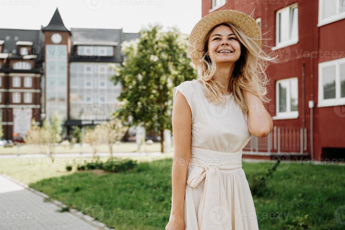 una bella bionda cammina per una città. donna in abito bianco foto