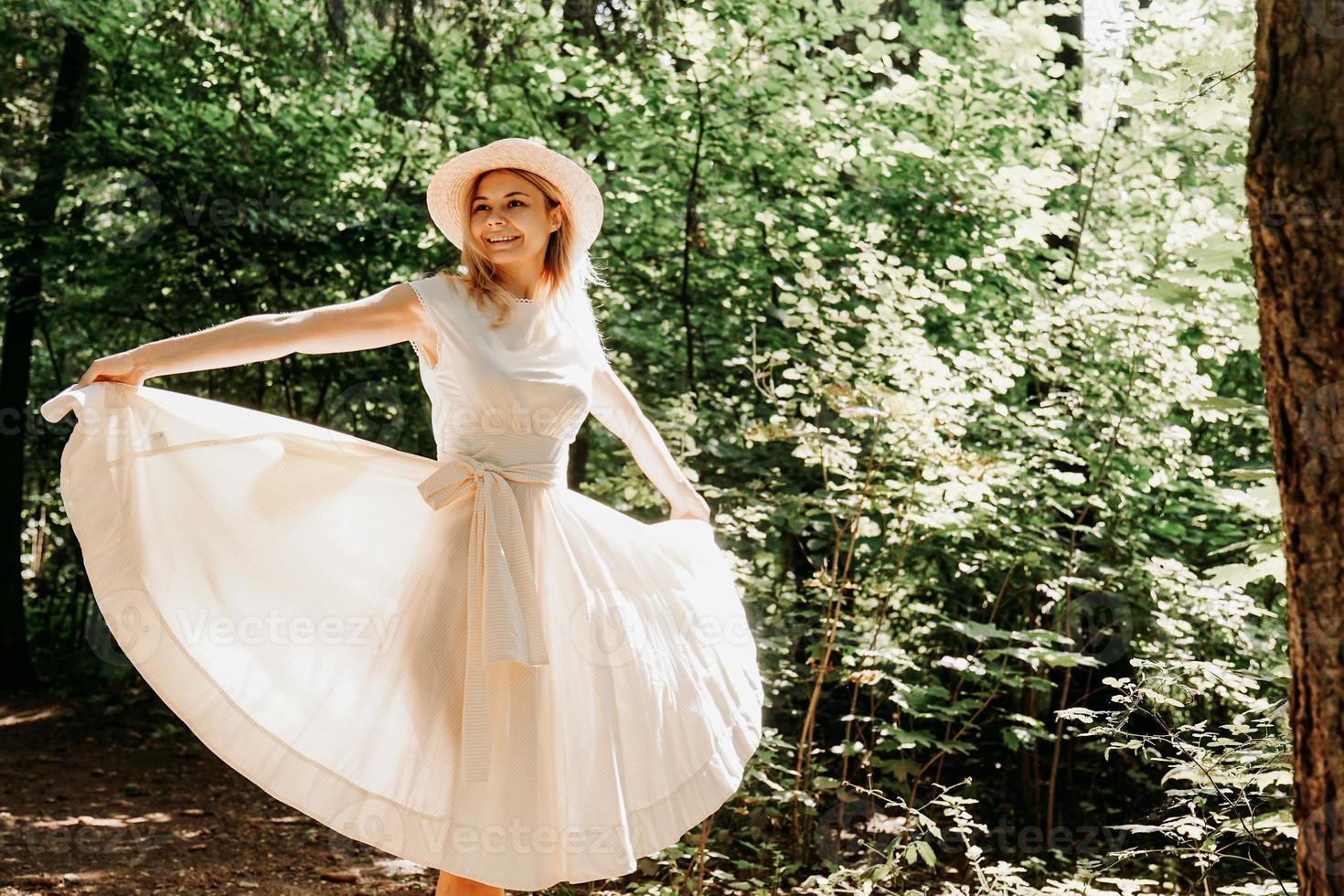 giovane donna con cappello di paglia che tiene l'orlo del suo vestito bianco foto