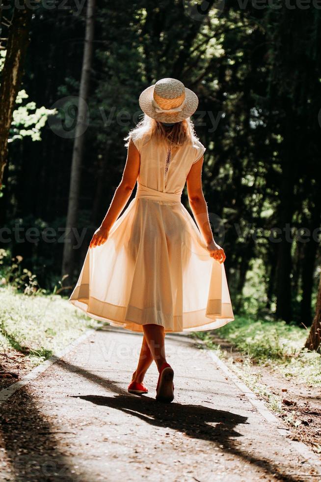 una giovane donna in abito bianco e cappello di paglia cammina nel bosco foto