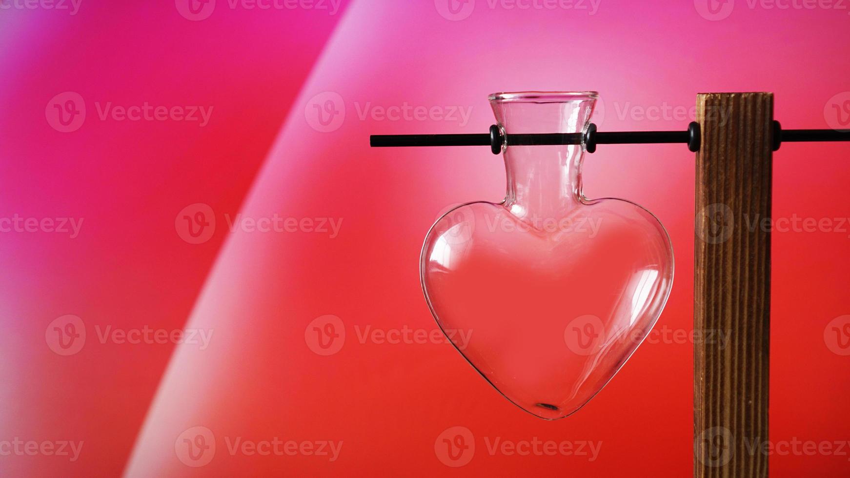 vaso di vetro vuoto a forma di cuore su supporto di legno su rosso foto