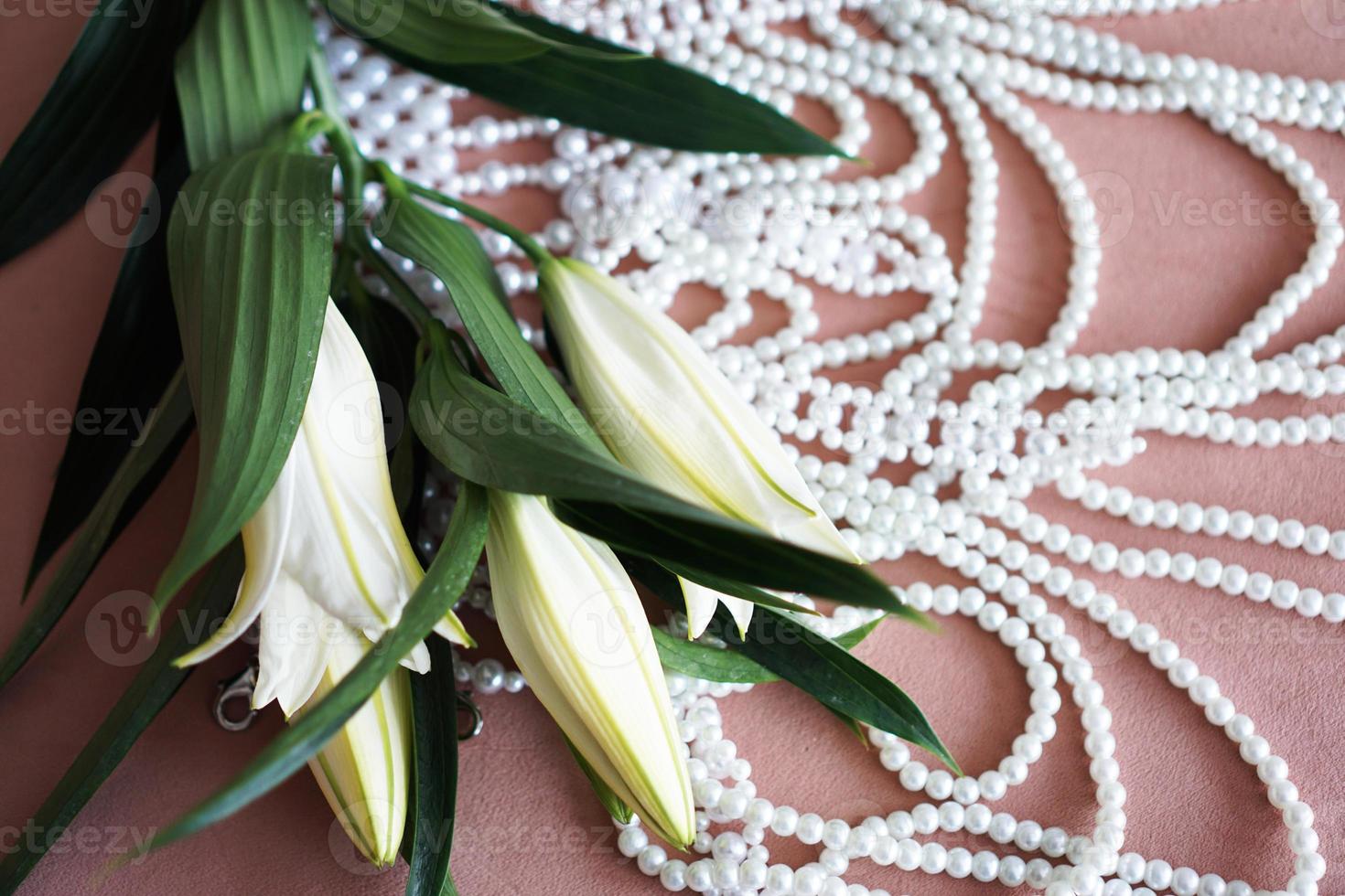 gigli bianchi e una collana di perle su fondo rosa. foto