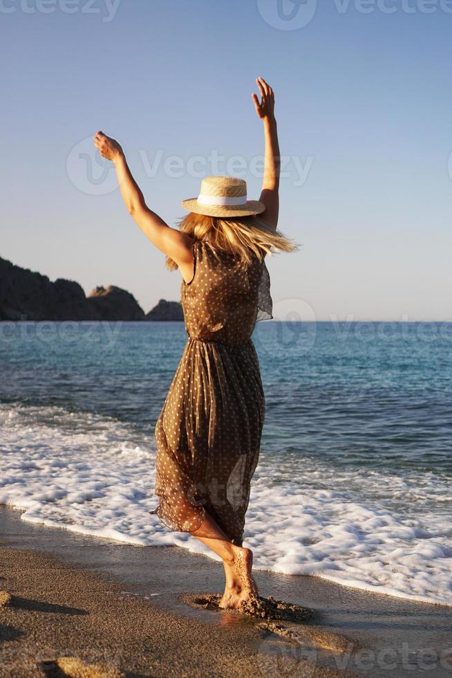 donna sulla spiaggia in un vestito marrone e con un cappello di paglia foto