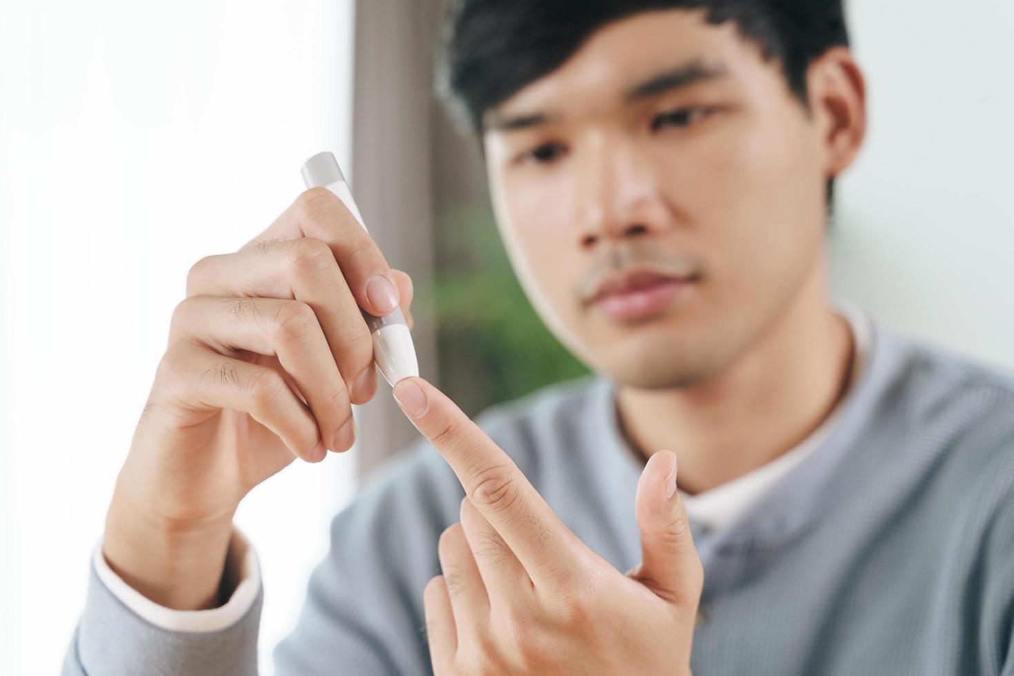 l'uomo usa la lancetta sul dito controllando il livello di zucchero nel sangue con il glucometro. foto