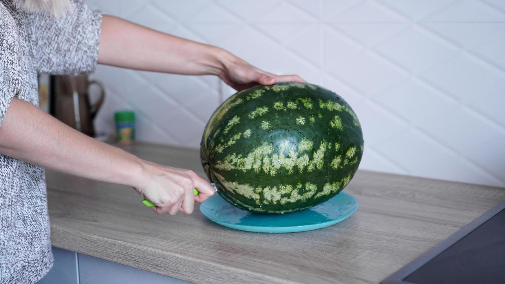 primo piano della donna che taglia a mano l'anguria in cucina foto