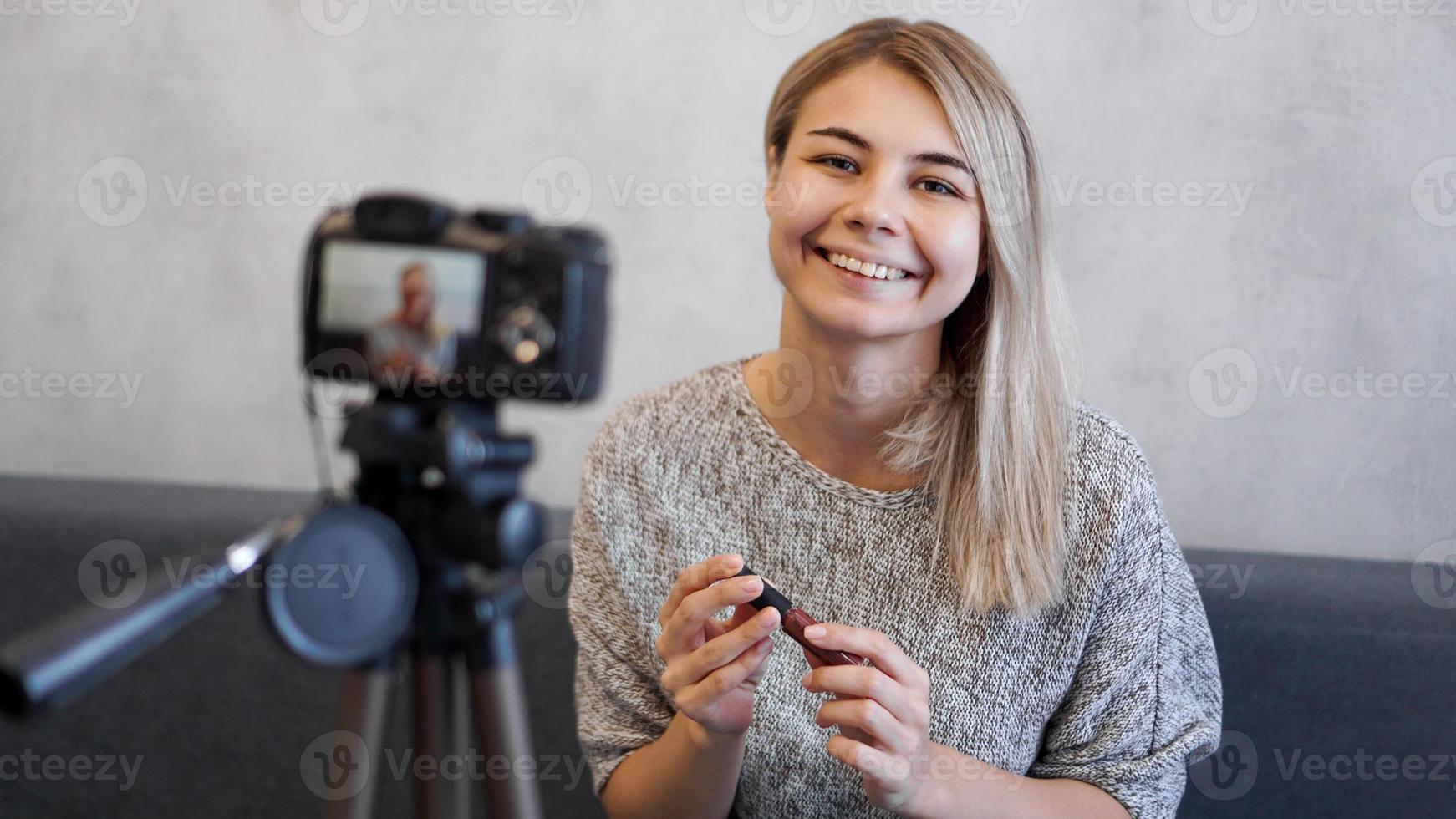 donna vlogger che mostra rossetto. blogger di bellezza in home studio foto