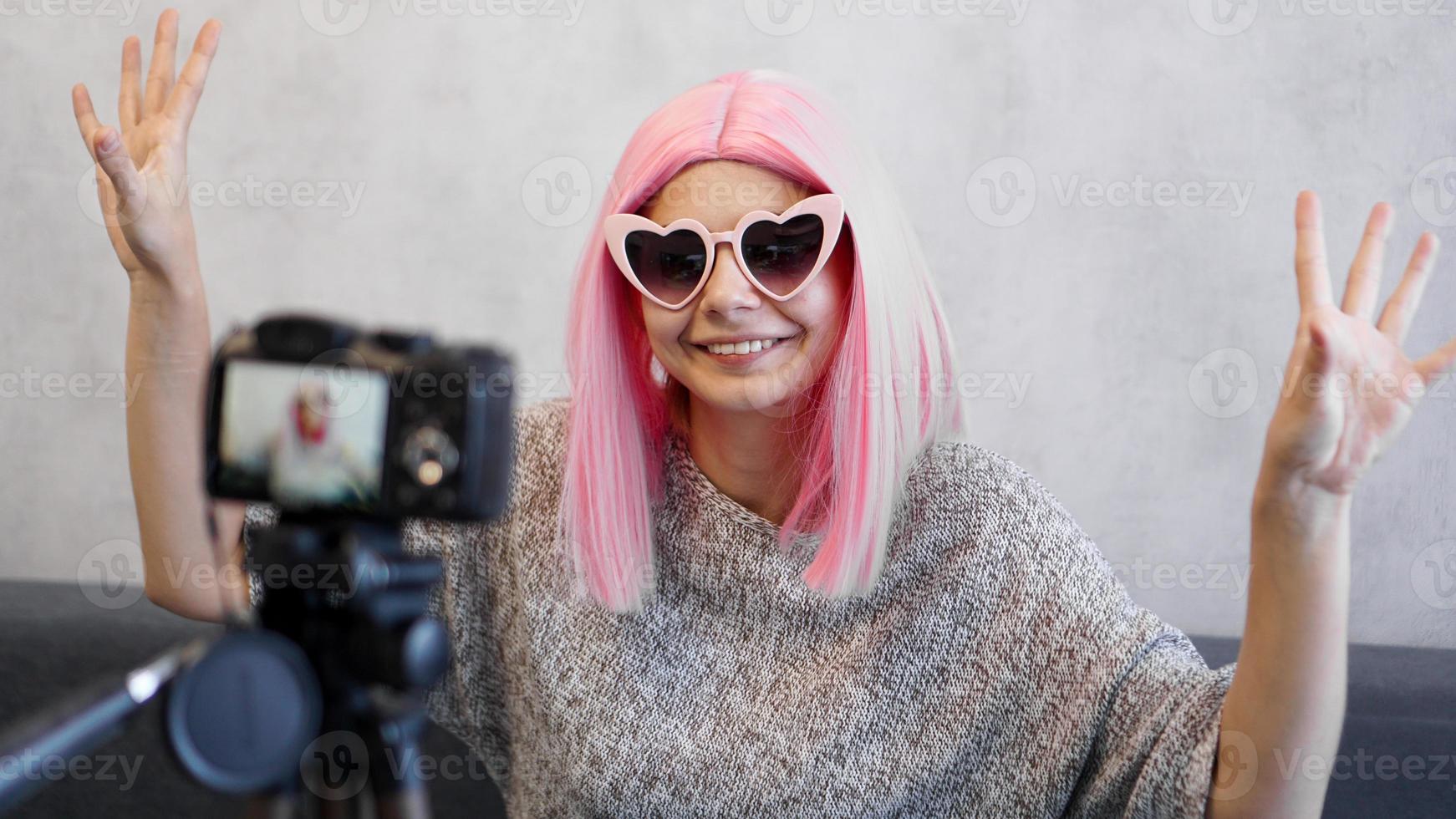 blogger ragazza felice in parrucche rosa davanti alla telecamera su un treppiede foto