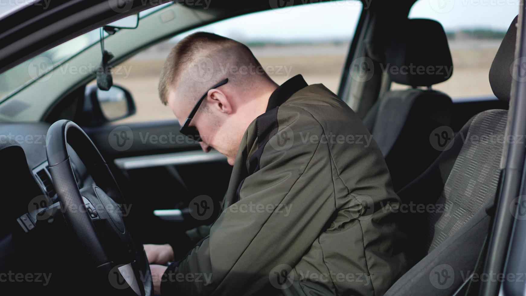 vista laterale del giovane uomo alla moda fiducioso in occhiali da sole nella sua auto foto