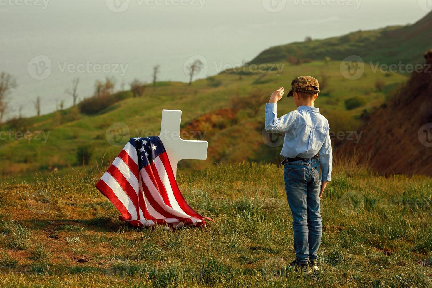 un ragazzo con un berretto militare saluta la tomba di suo padre foto