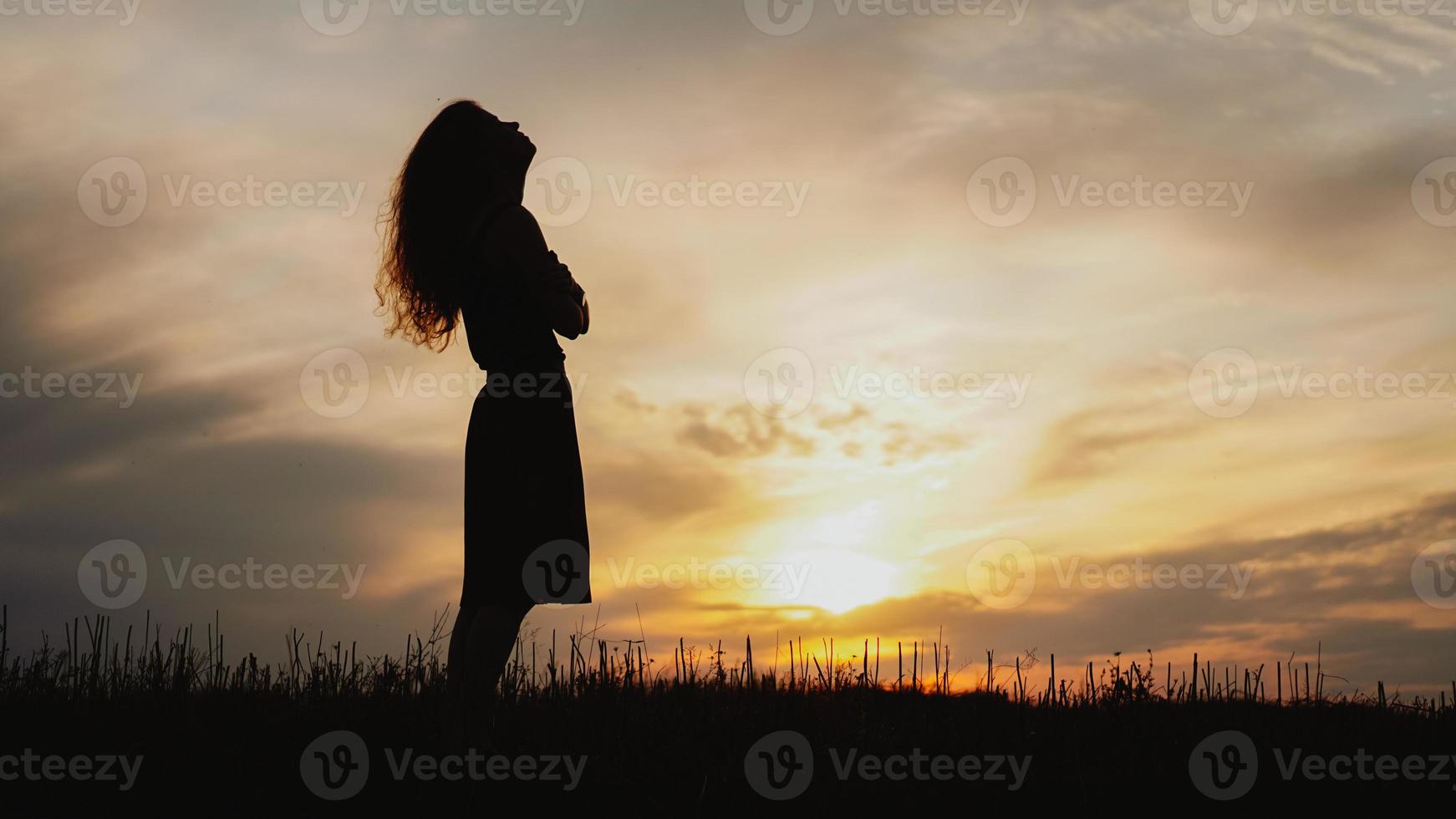 silhouette di una giovane donna in piedi in un campo di erba secca al tramonto? foto