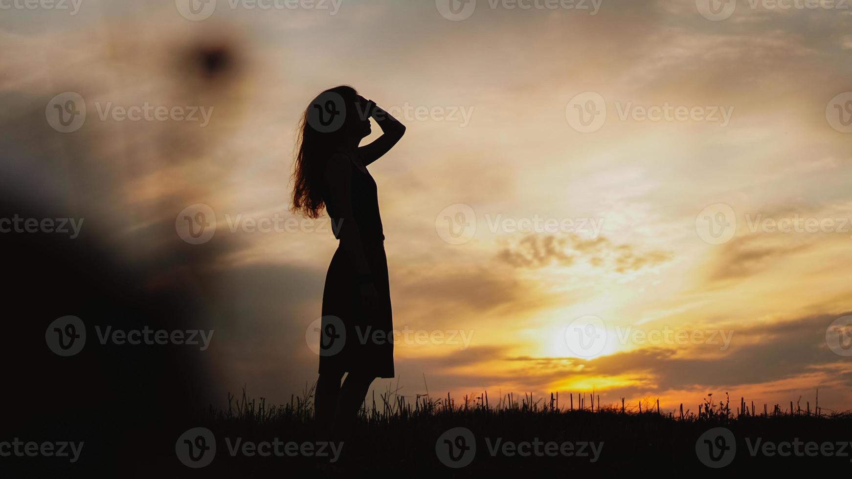 silhouette di una giovane donna in piedi in un campo di erba secca al tramonto? foto