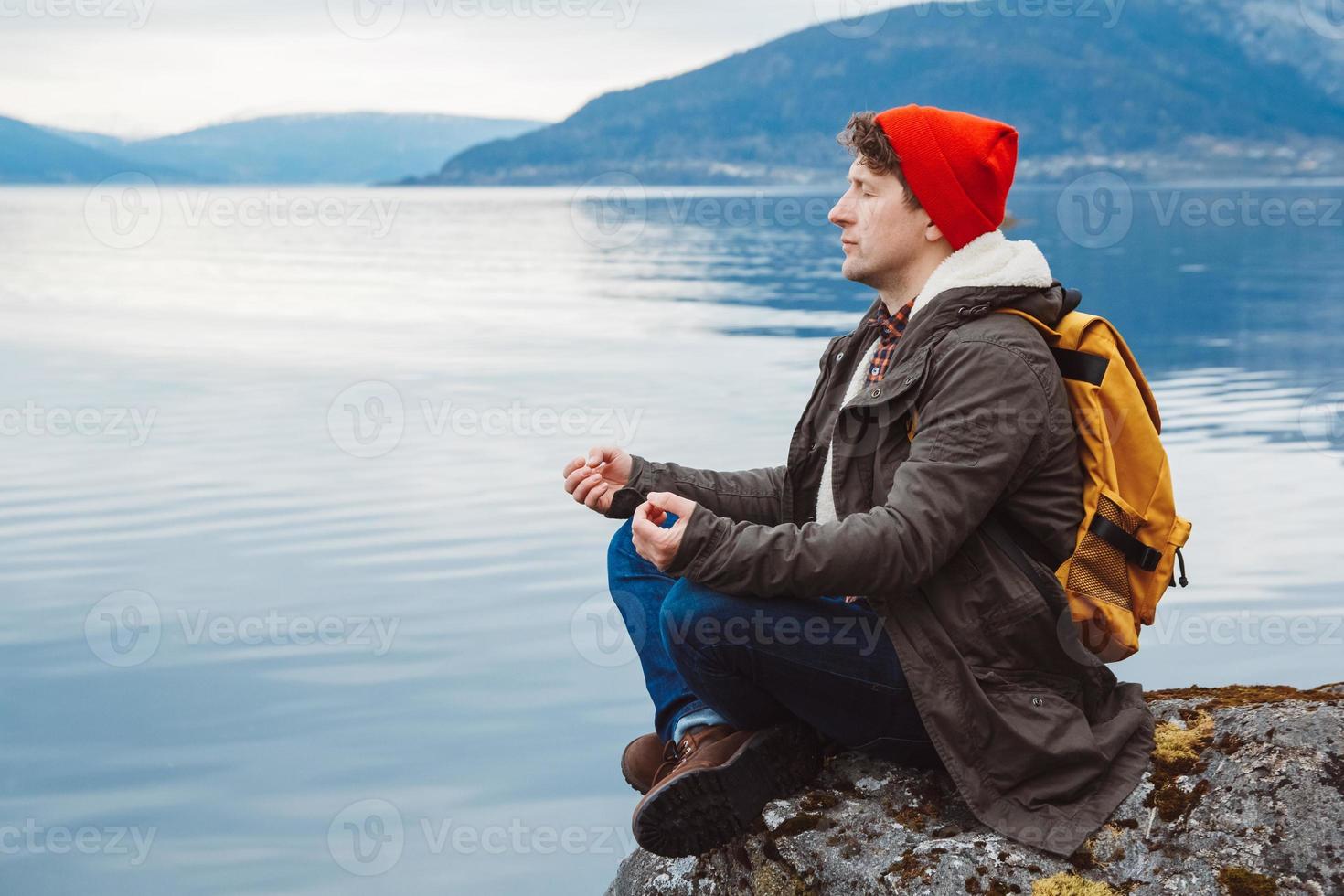 uomo viaggiatore in posizione meditativa seduto su una spiaggia rocciosa foto