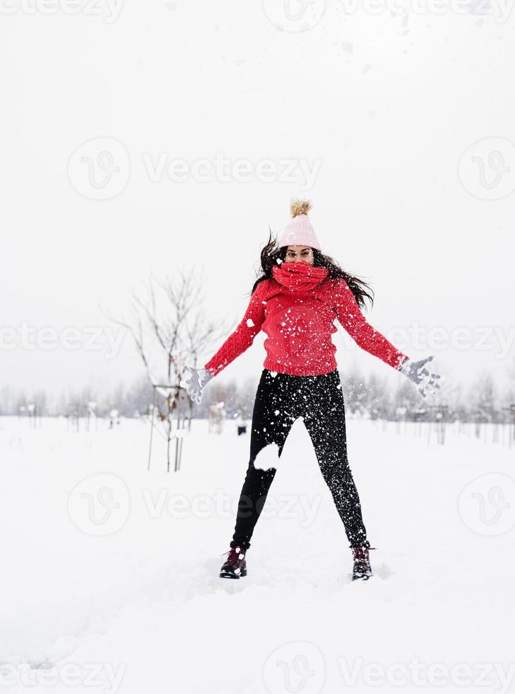 giovane donna bruna spensierata in maglione rosso che salta nella neve all'aperto foto