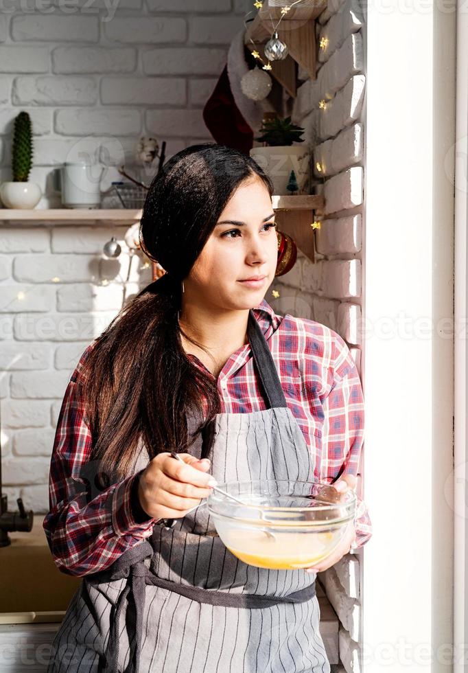 giovane donna latina che sbatte le uova cucinando in cucina foto