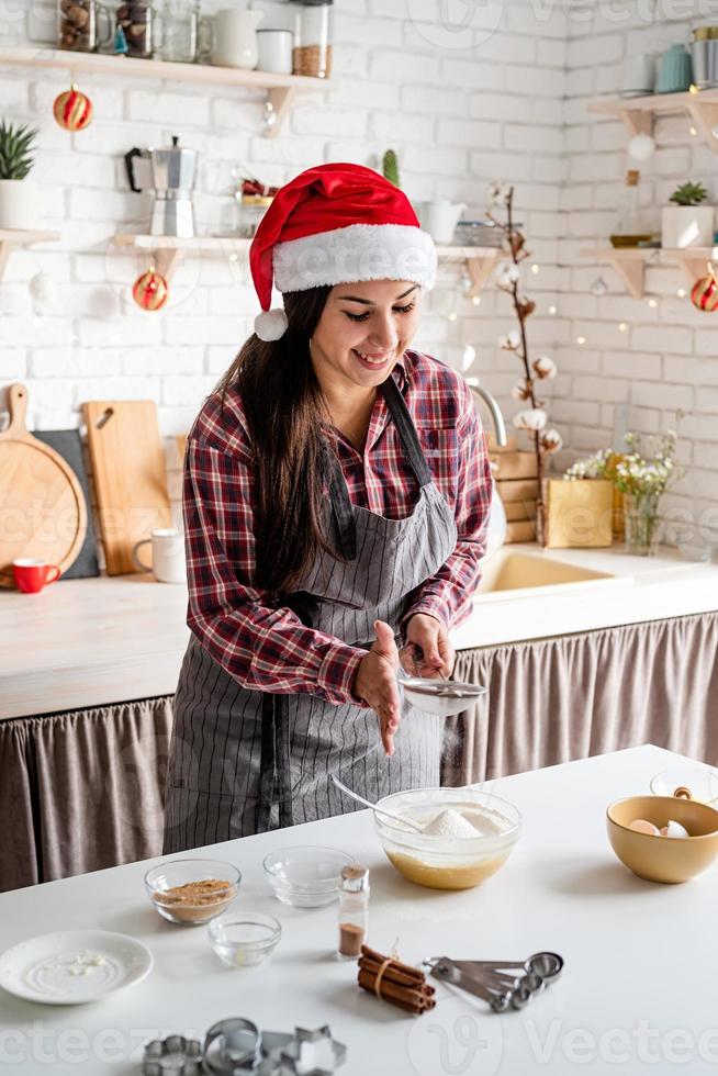 giovane donna latina che versa la farina all'impasto che cucina in cucina foto