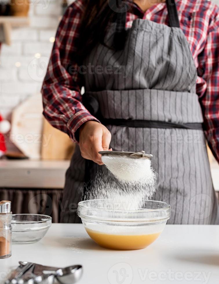 giovane donna latina che versa la farina all'impasto che cucina in cucina foto