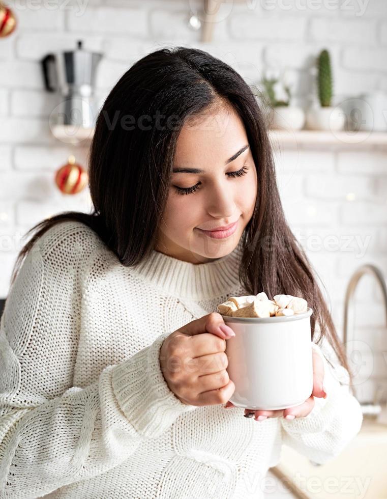 donna bruna che tiene una tazza di cacao marshmallow in cucina foto