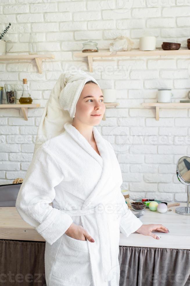 felice giovane donna che applica uno scrub per il viso sul viso nella sua cucina di casa foto