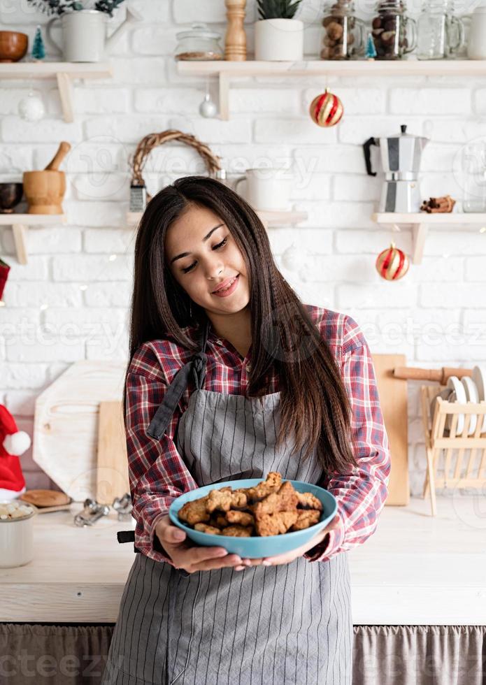 donna in grembiule che tiene un piatto con biscotti fatti in casa in cucina foto