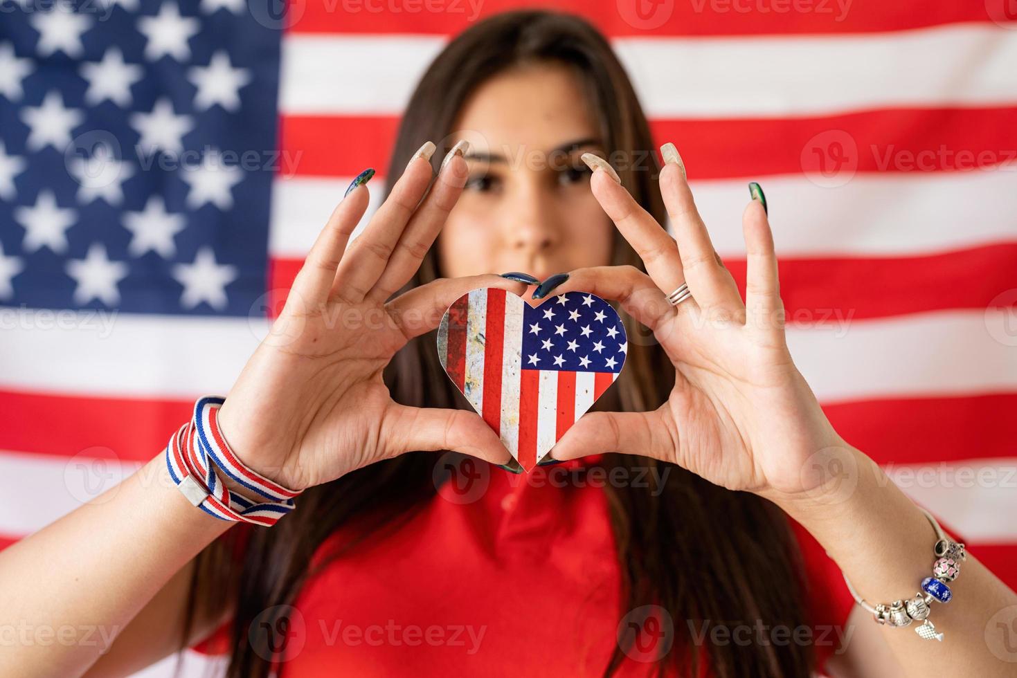 donna che tiene una bandiera nazionale a forma di cuore sullo sfondo della bandiera degli Stati Uniti foto