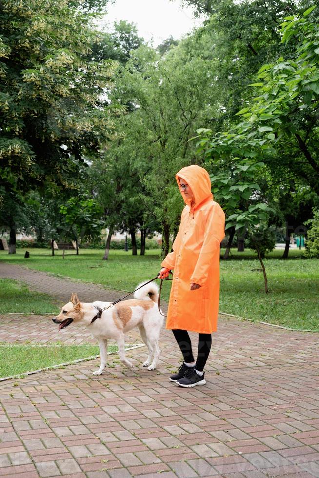 giovane donna in impermeabile arancione che cammina con il suo cane in un parco foto