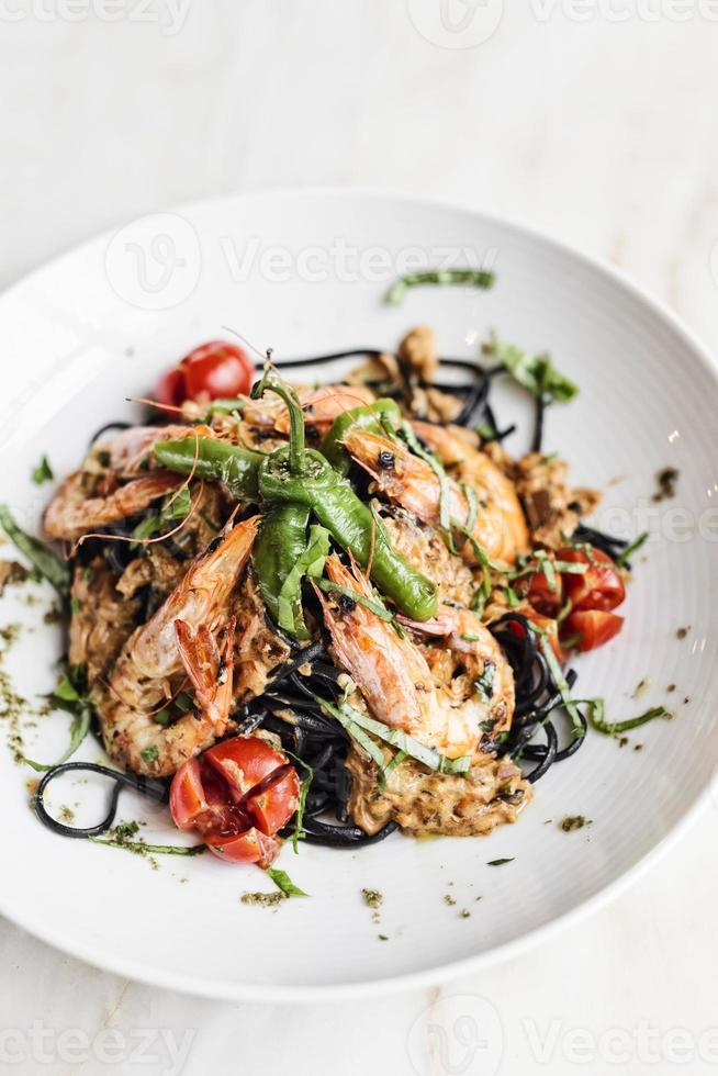 cibo gourmet gamberi alla griglia e verdure su pasta al nero di seppia foto