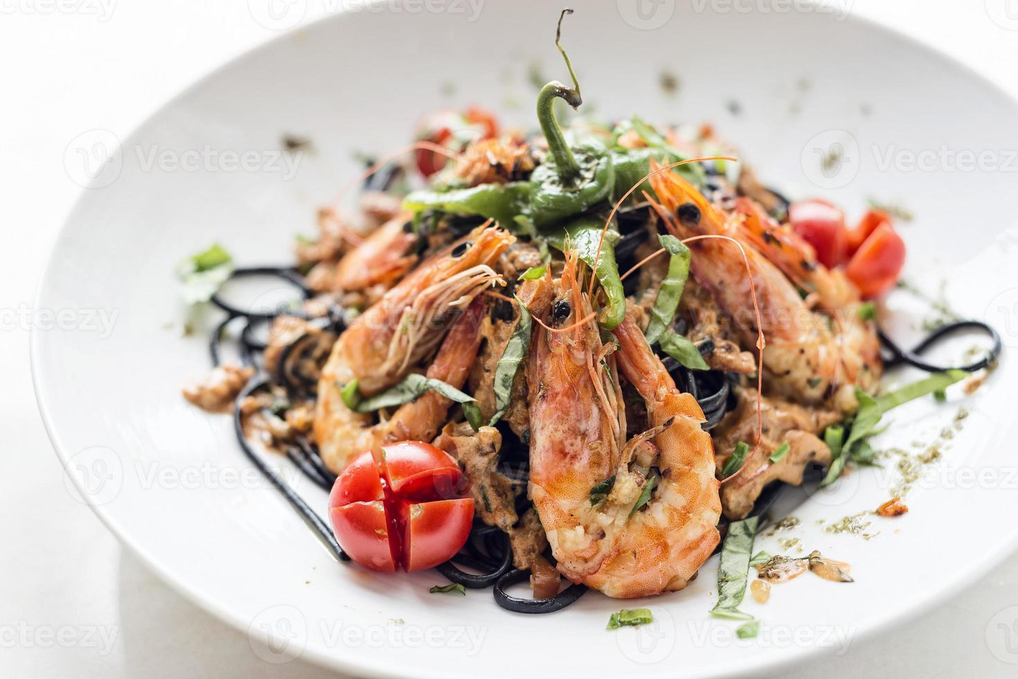 cibo gourmet gamberi alla griglia e verdure su pasta al nero di seppia foto